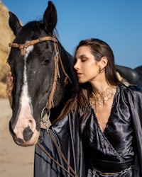 a woman in a black dress standing next to a horse