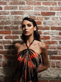 a woman in an orange and black dress posing in front of a brick wall