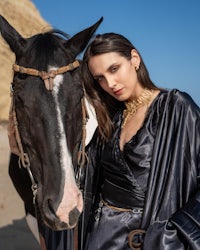 a woman is posing with a horse on the beach