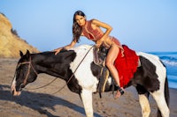 a woman in a red dress riding a horse on the beach
