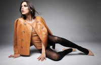 a woman in a tan leather jacket posing on the floor