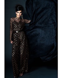 a woman in a black and gold jumpsuit posing on a black background
