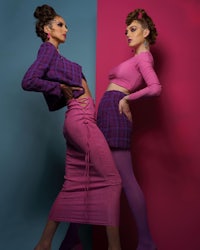 two women are posing in front of a pink and blue wall