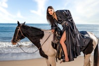 a woman in a black dress riding a horse on the beach