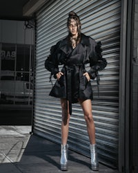 a woman in a black trench coat posing in front of a garage