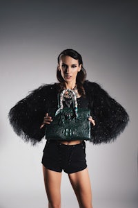 a woman is holding a green crocodile bag