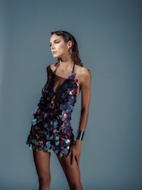 a woman in a colorful sequin dress posing on a gray background