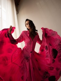 a woman in a pink dress is posing in front of a window
