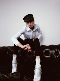 a woman wearing a hat and white shirt sitting on a black couch