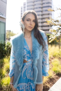 a woman wearing a blue dress and fur vest