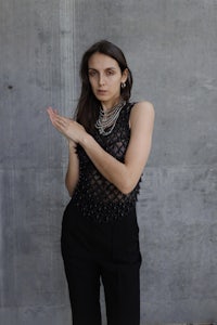 a woman wearing a black top and pants posing in front of a concrete wall