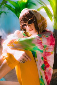 a woman wearing sunglasses and a yellow jacket sitting on the ground