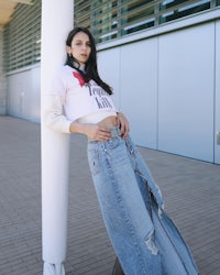 a woman in a denim skirt leaning against a pole