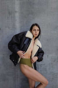 a woman posing in a black jacket and green bikini