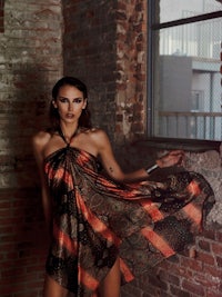 a woman in an orange and black dress posing in front of a brick wall