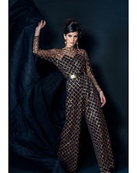 a woman in a black and gold jumpsuit posing on a black background