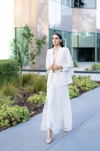 a woman in a white blazer and skirt walking down a sidewalk
