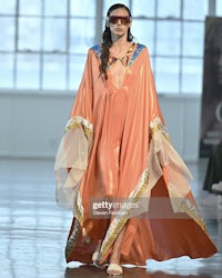 a model walks the runway wearing an orange cape and sunglasses during london fashion week spring/summer 2018 in london