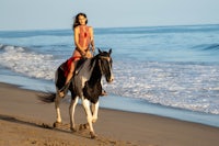 a woman riding a horse on the beach