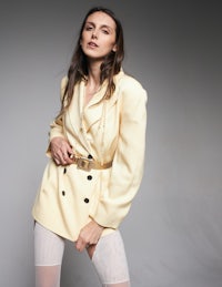 a woman in a yellow blazer and stockings posing for a photo