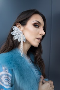 a woman wearing a blue fur coat and earrings