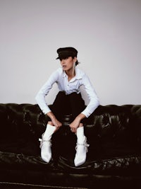 a woman sitting on a black couch wearing a hat and white shoes