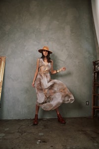 a woman in a dress and hat poses in front of a mirror