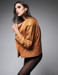 a woman in a tan leather jacket posing on a gray background